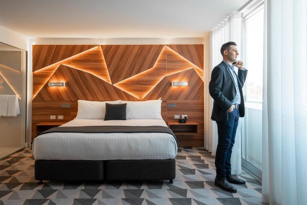 Habitación de hotel moderna con cabecera de diseño geométrico, una cama grande y vistas al exterior.