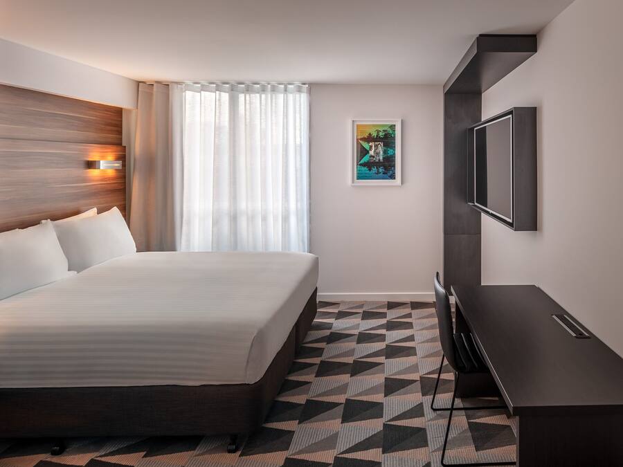 A hotel room with a bed, a TV, a painting, and a geometric patterned floor.