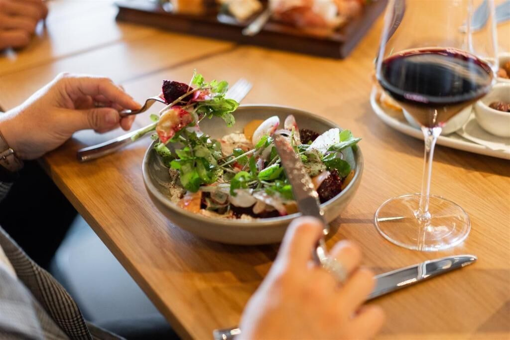 A dining table with a salad bowl, a wine glass, and a fork.