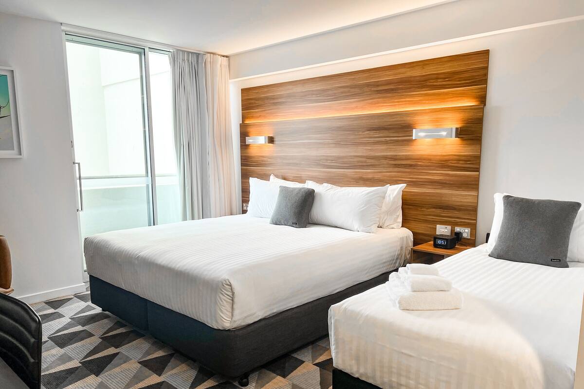Habitación de hotel con dos camas, un cabecero moderno, suelo estampado y vistas por la ventana.
