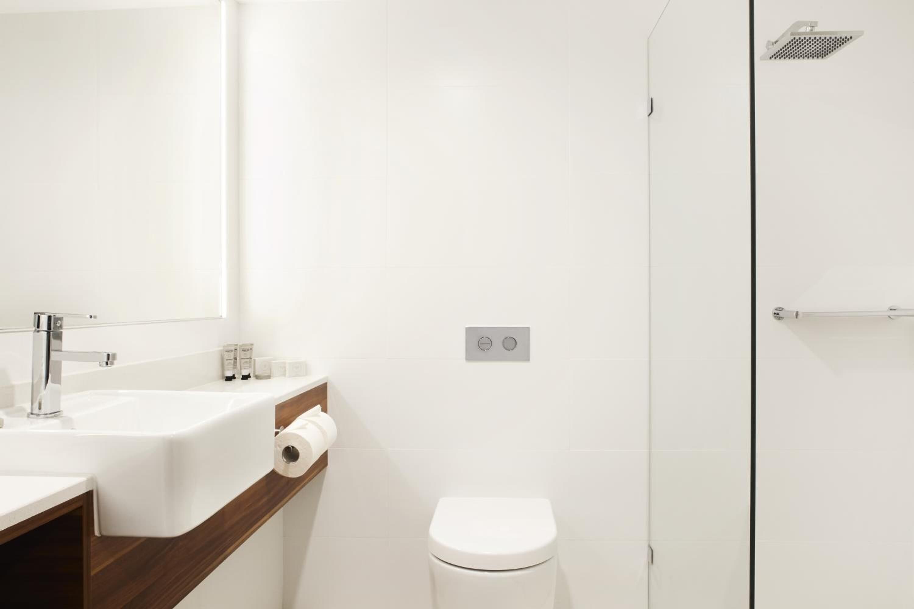 Un baño moderno con un lavamanos, espejo y retrete blancos.