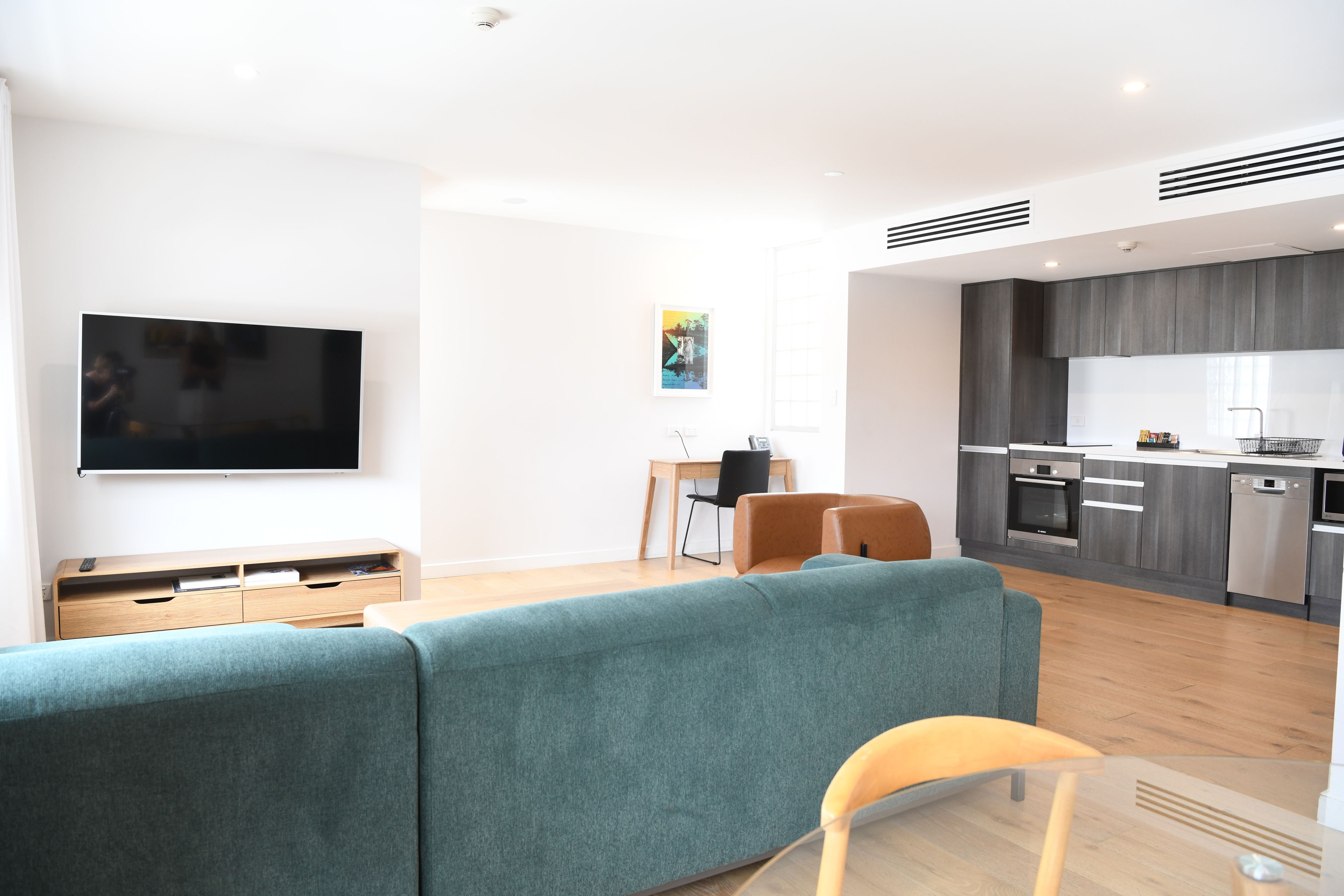 Een moderne woonkamer met een grote flatscreen televisie, een blauwgroene bank en een klein houten bijzettafeltje.