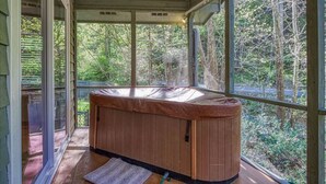 Un bain à remous situé dans un espace extérieur abrité, doté de grandes fenêtres et offrant une vue sur la forêt environnante.
