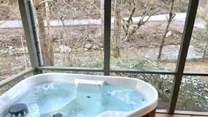 Un bain à remous avec un revêtement extérieur en bois, un petit marchepied permettant d’y accéder, et une vue sur un paysage enneigé à travers de grandes fenêtres.