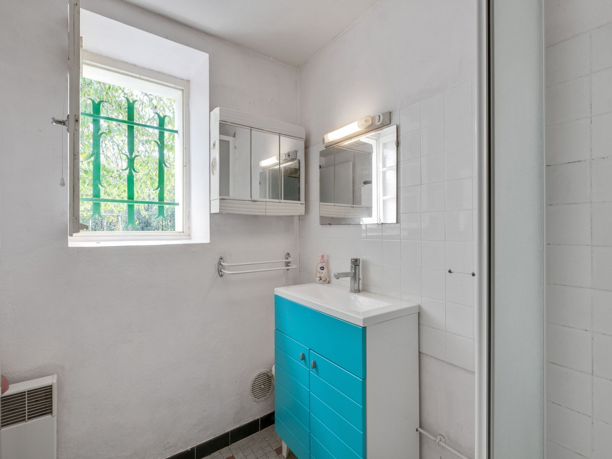 Ein Badezimmer mit Fenster, Waschbecken, Spiegel und einem blauen Schrank.