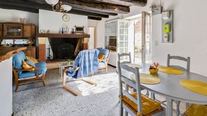 A rustic room with exposed wooden beams, a fireplace, a dining table with yellow placemats, and a cozy seating area with blue cushions.