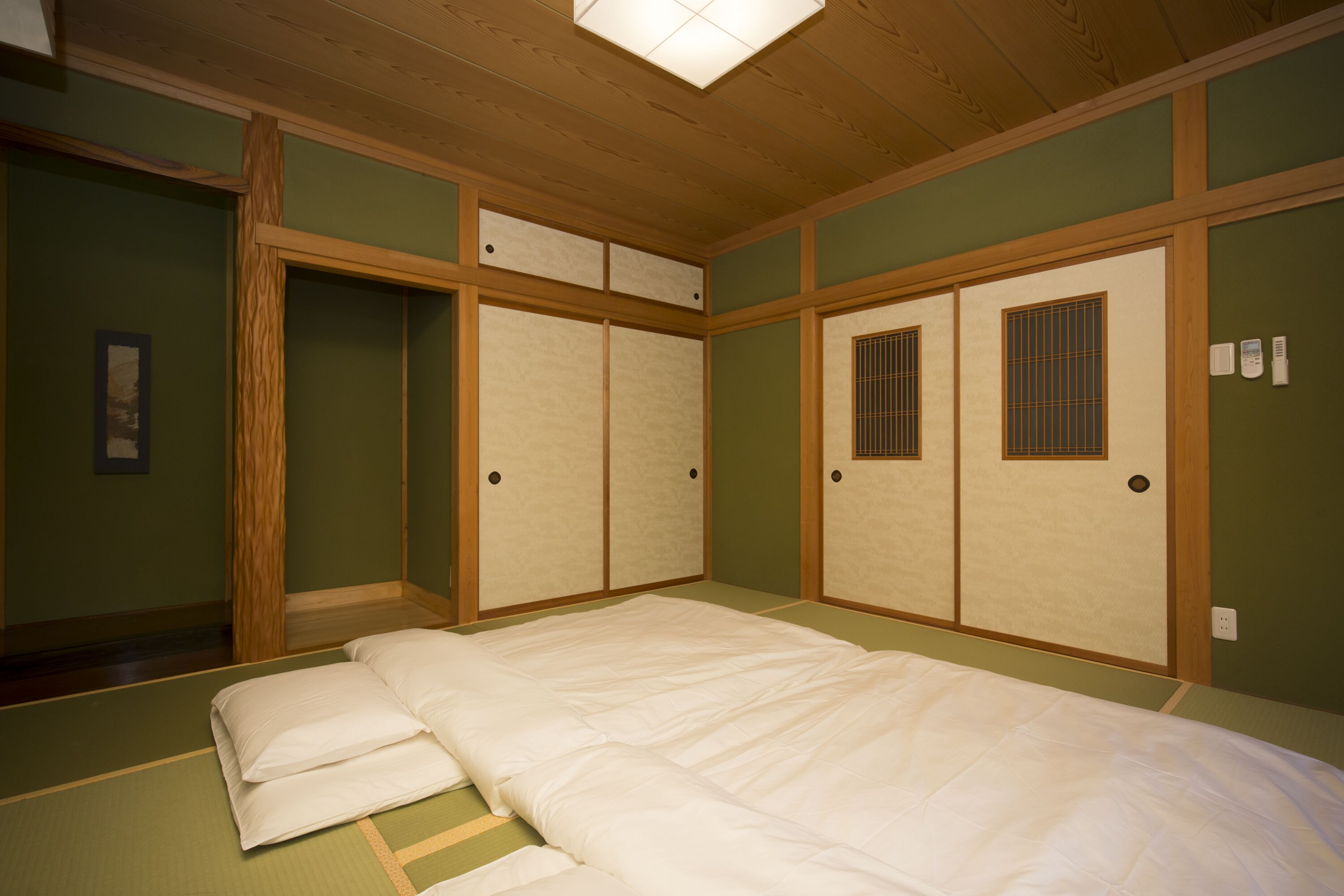 A traditional Japanese-style room with tatami flooring, a low wooden bed, sliding doors, and a ceiling light fixture.