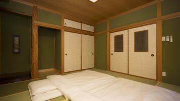 A traditional Japanese-style room with tatami flooring, a low wooden bed, sliding doors, and a ceiling light fixture.