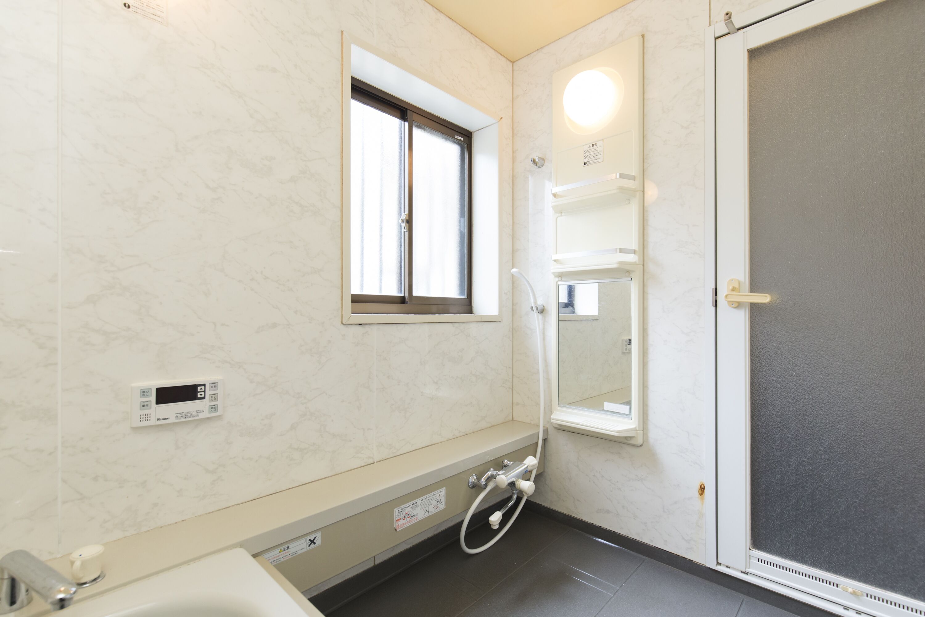 A bathroom with a toilet, sink, and shower area. There is a window and a control panel on the wall.