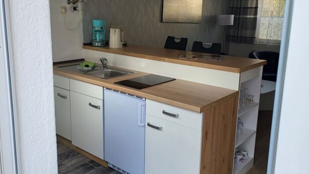Uma cozinha compacta com máquina de lavar louça embutida, cafeteira e micro-ondas.