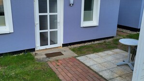 Um pequeno edifício térreo com fachada azul, porta branca e janela com persianas.