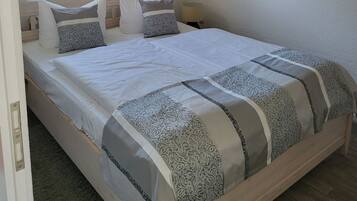 Una cama bien hecha con ropa de cama y almohadas estampadas, una lámpara de noche y una ventana con persianas.