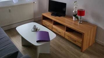 Ein modernes Wohnzimmer mit einem weißen Sofa, einem Holz-TV-Schrank, einem Flachbildfernseher, einer roten Lampe und einer kleinen Topf-Orchidee.