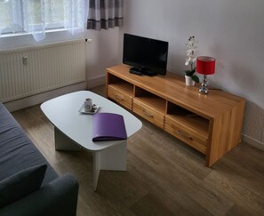 A modern living room with a white sofa, a wooden TV stand, a flat-screen TV, a red lamp, and a small potted orchid.