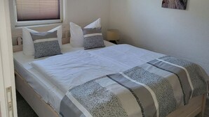 Cama bem arrumada com colcha estampada e travesseiros, luminária de cabeceira e janela com persianas.