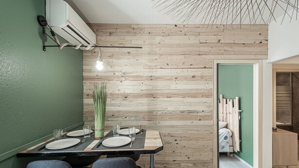 Ein Essbereich mit Holzwand, einer grünen Tür und einer modernen Leuchte.