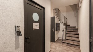 Ein moderner Flur mit einer dunklen Tür, einem Kartenlesegerät für Zutrittskarten und einer Treppe mit Holzstufen und einem Metallgeländer.