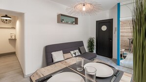 Ein modernes Wohnzimmer mit einem dunkelgrauen Sofa, einem Holzesstisch gedeckt mit Tellern und Gläsern, einer Pendelleuchte und einer kleinen Pflanze.