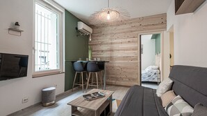 Ein kompakter Wohnraum mit einer Couch, einem kleinen Esstisch mit Stühlen, einem an der Wand montierten Fernseher und einer Wand in Holzoptik.