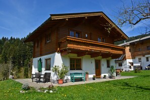 A wooden chalet with a balcony, a patio with a table and chairs, and a green bench. - Ferienwohnung Gaßoidhof OG (Fieberbrunn)