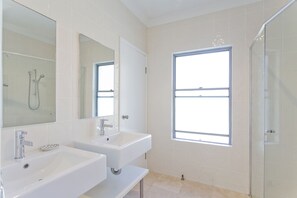 A bathroom with two sinks, a shower, and a window.