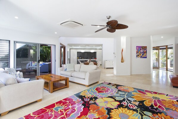 A spacious living room with a large floral rug, a white sofa, a wooden coffee table, and a ceiling fan.