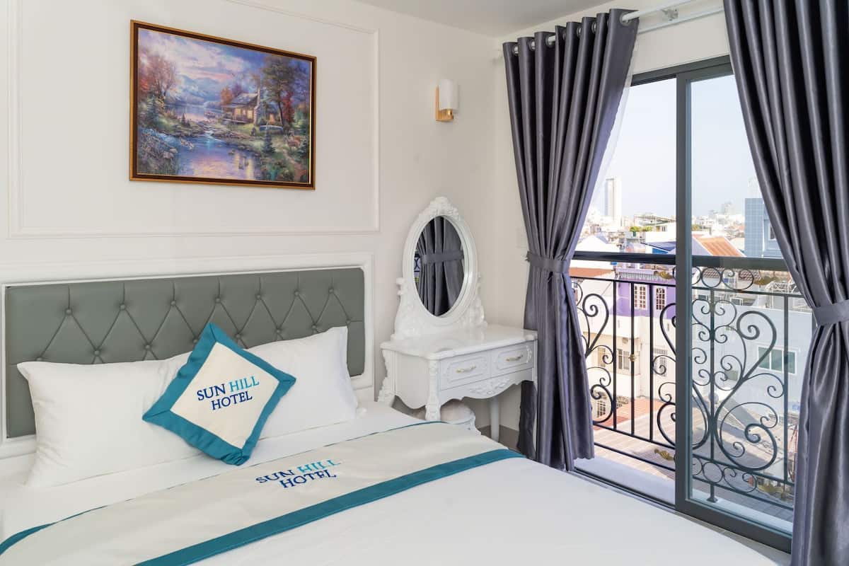 Ein Hotelzimmer mit Bett, einem Gemälde, einem Schminktisch und einem Spiegel, sowie einem Balkon mit Aussicht.