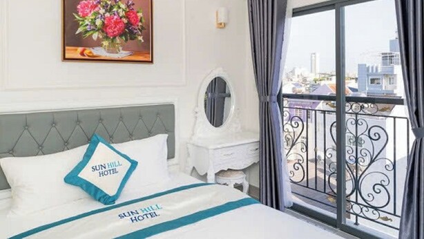 Une chambre d’hôtel comprenant un lit, une table de chevet, un miroir, une œuvre d’art florale encadrée et un balcon avec vue sur la ville.