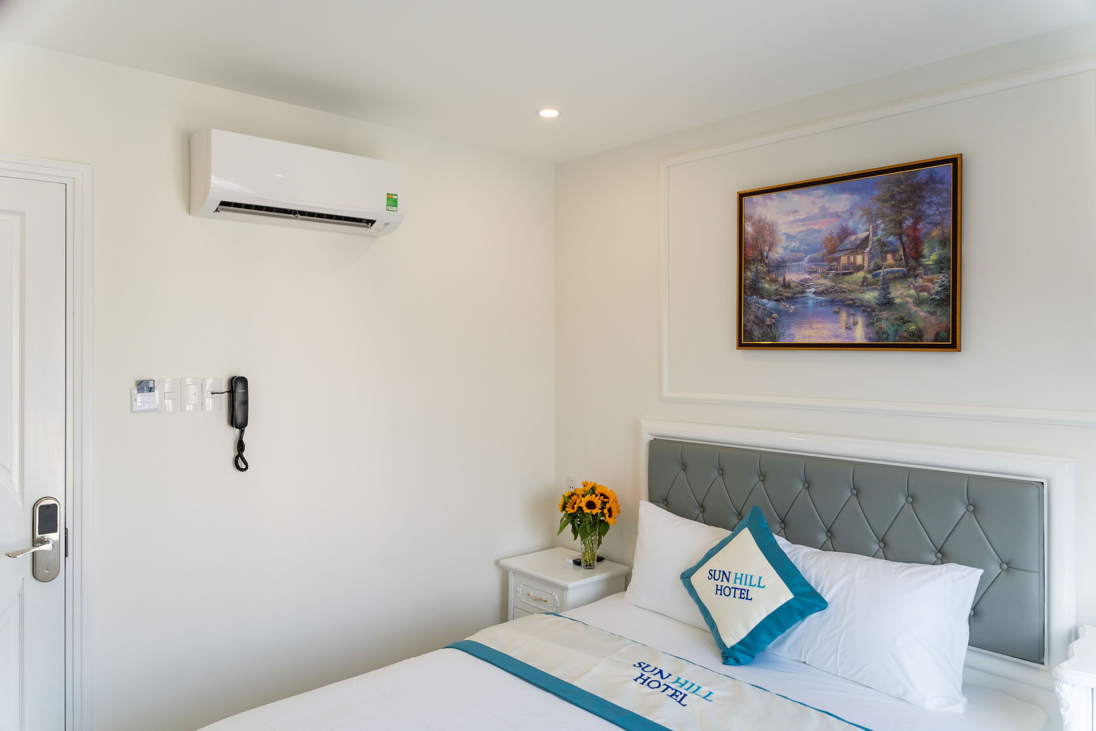 Une chambre d’hôtel avec un lit, une table de chevet avec un téléphone, un climatiseur et un tableau au mur.
