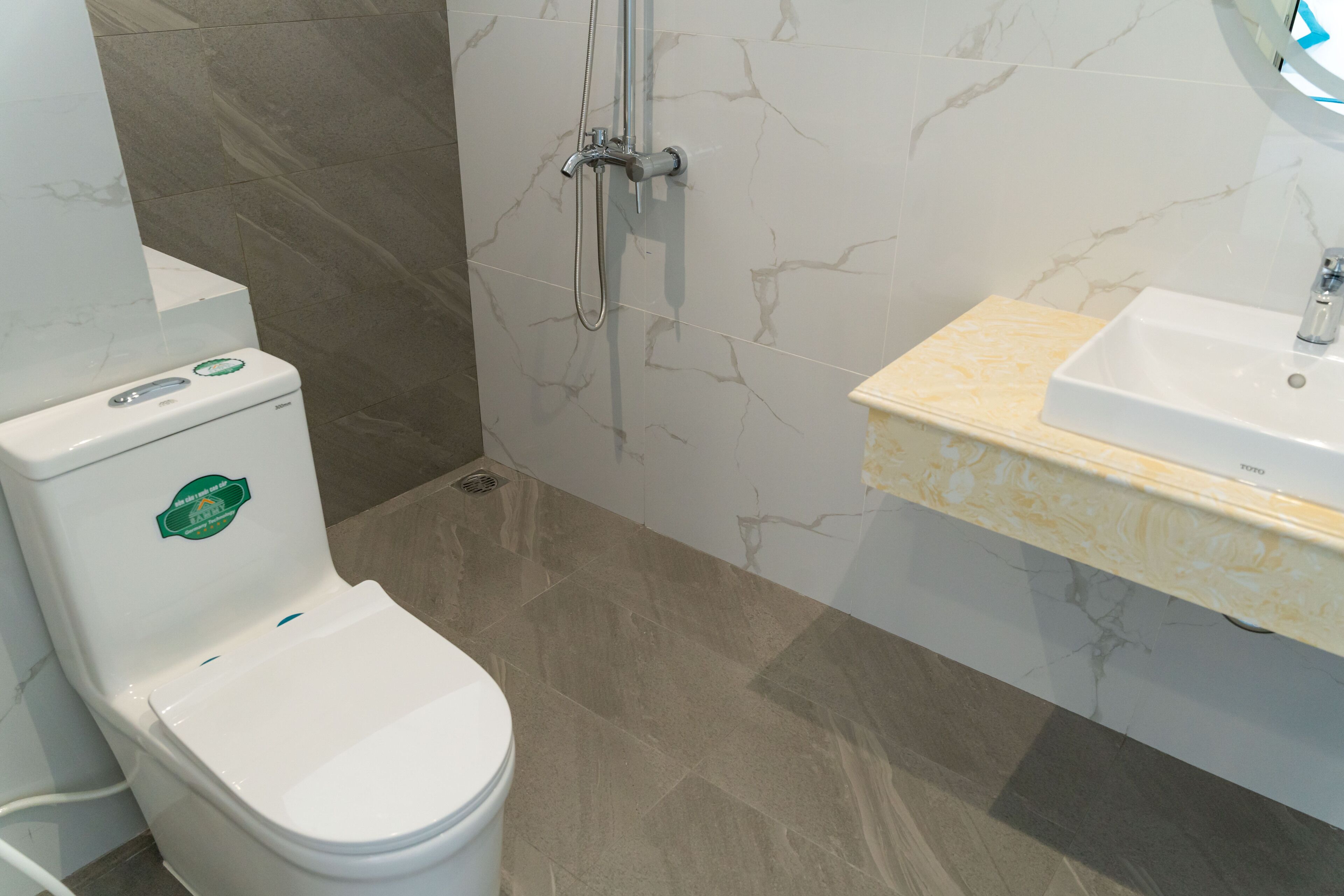 A bathroom with a white toilet, a shower with a handheld showerhead, and a sink with a marble countertop.