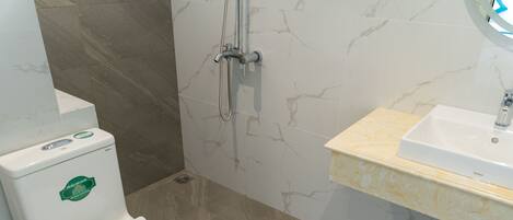 A bathroom with a white toilet, a shower with a handheld showerhead, and a sink with a marble countertop.