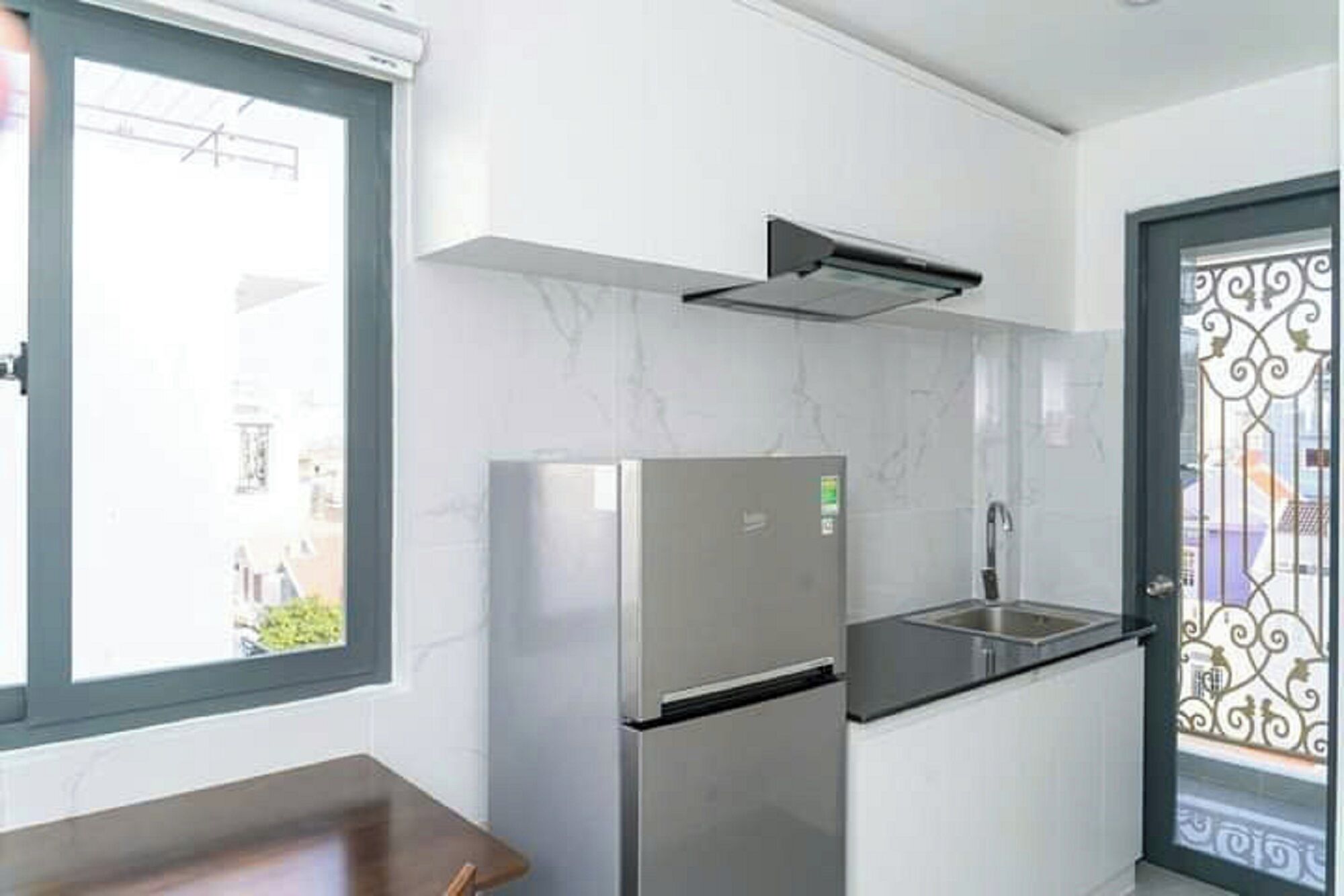 A compact kitchen with a stainless steel refrigerator, a sink, and a window providing natural light.