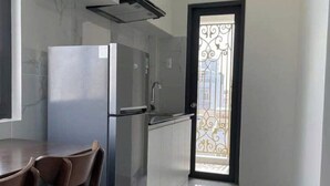 Une cuisine moderne équipée d’un réfrigérateur, d’une cuisinière et d’un évier. On y trouve une table à manger avec des chaises. Le sol est carrelé et les murs sont blancs.