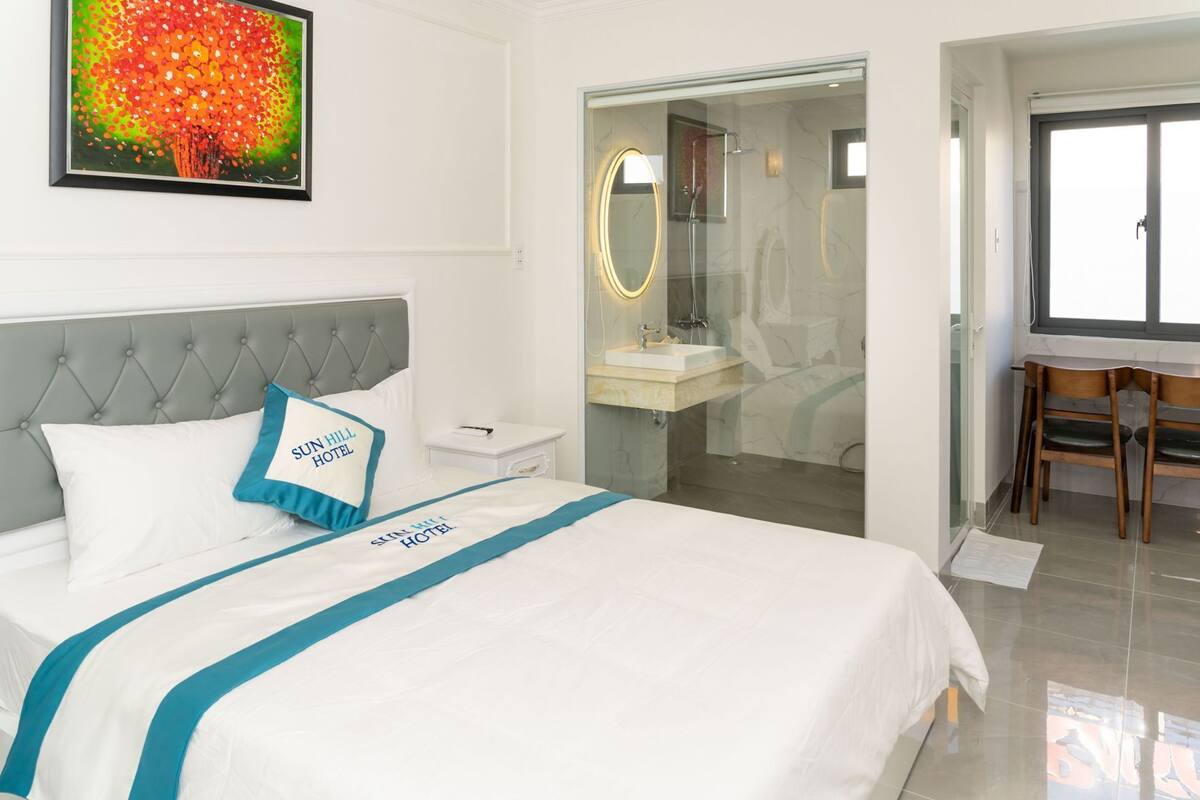 Ein Hotelzimmer mit Bett, Nachttisch, Badezimmer mit Duschkabine aus Glas und einem Essbereich mit Stühlen.