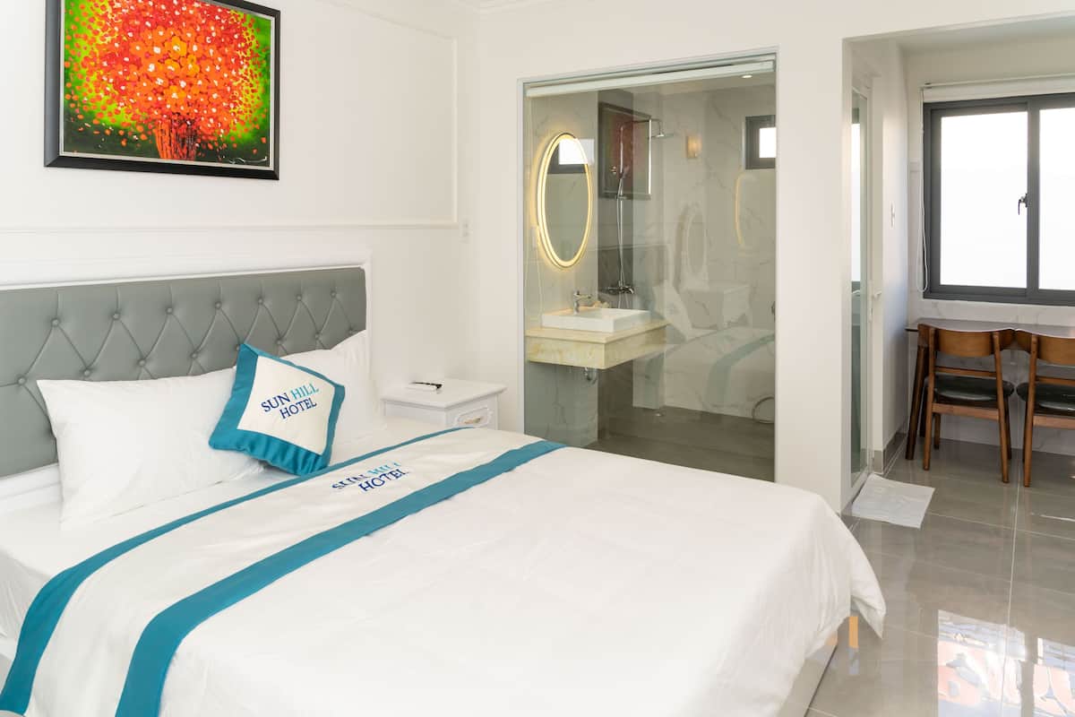 Ein Hotelzimmer mit Bett, Badezimmer mit Duschkabine, Schreibtisch mit Stuhl und Fenster.