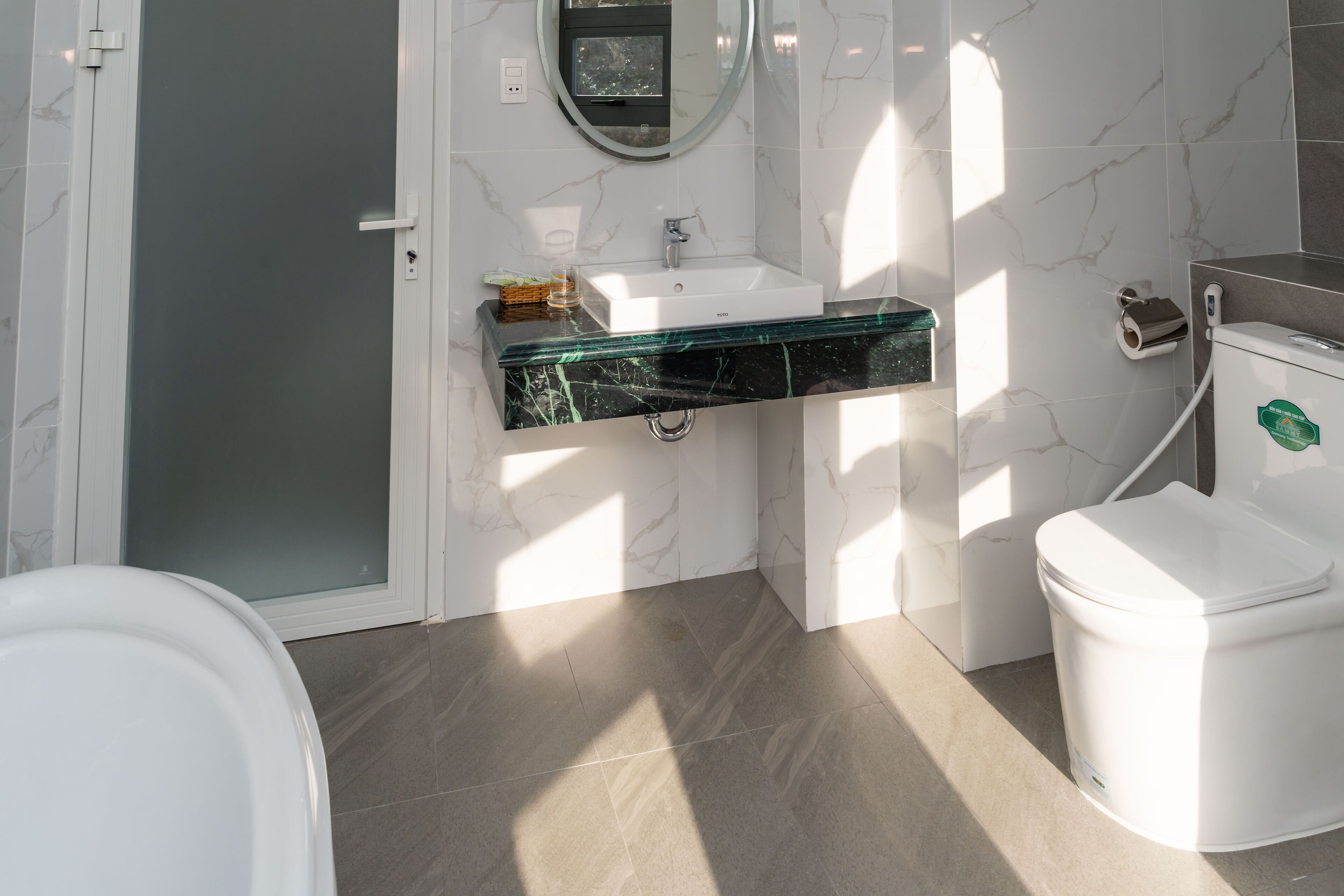 Un baño moderno con lavamanos de cristal, inodoro blanco y paredes de mármol.