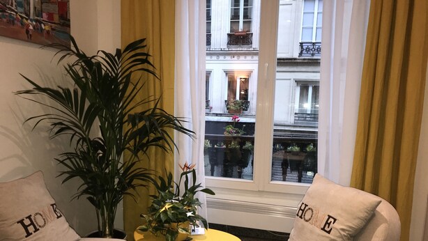 Una habitación acogedora con dos sillones color beige, una mesa amarilla y una planta grande en maceta.
