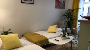 Una habitación de hotel pequeña y acogedora con dos camas individuales, una mesita y una planta en maceta.