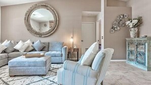 Un soggiorno con un divano beige, uno specchio rotondo e un elemento decorativo a parete.