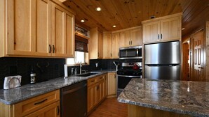 Una cocina con gabinetes de madera, encimeras de granito, electrodomésticos de acero inoxidable y salpicadero de azulejos negros.