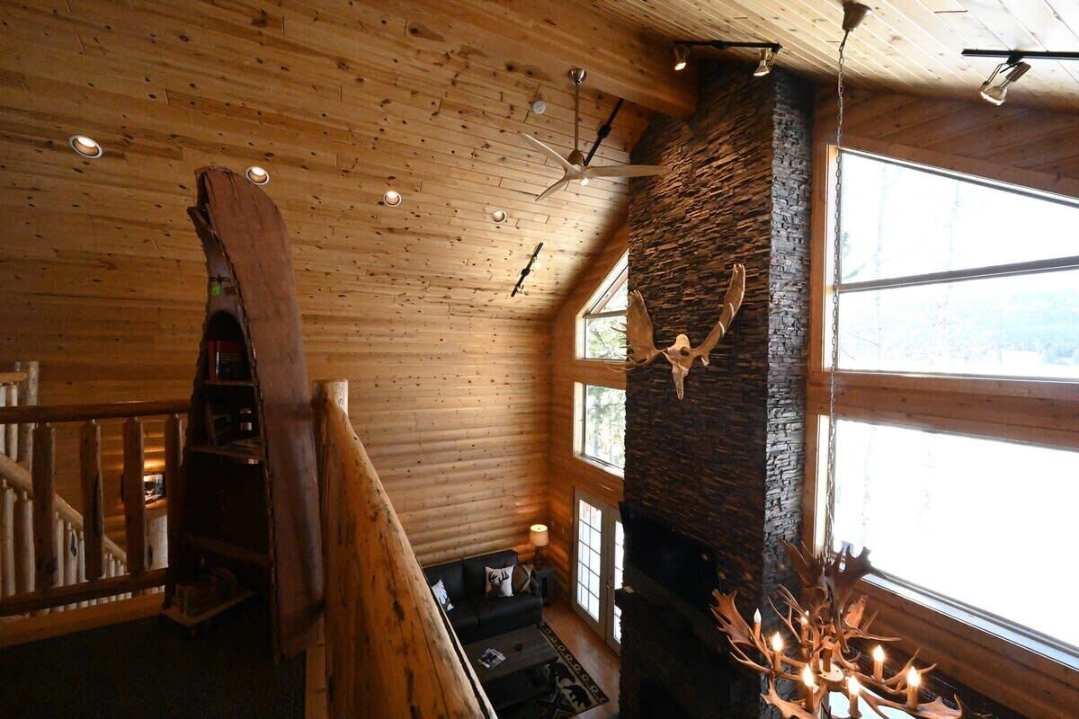 Un intérieur en bois avec une cheminée en pierre, un ventilateur de plafond et une grande fenêtre.