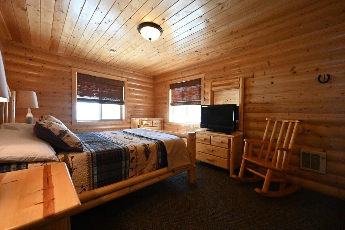 Una habitación de cabaña de madera con una cama, un televisor, un sillón mecedor y un escritorio.