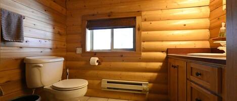 A wooden cabin bathroom with a toilet, sink, and window.