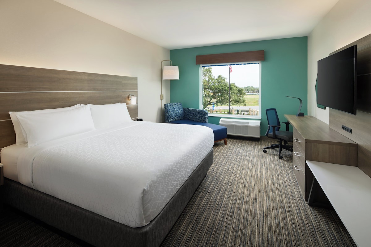 Une chambre d’hôtel avec un grand lit, un bureau avec une chaise, une télévision et une fenêtre donnant sur l’extérieur.