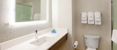 Un bagno con un lavandino bianco, uno specchio e un water. Asciugamani appesi al muro e cabina doccia in vetro.