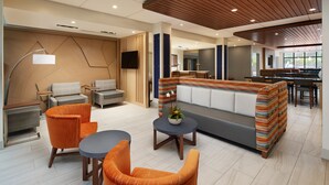 A modern hotel lobby with a sofa, chairs, a dining area, and a television. - HOLIDAY INN EXPRESS & SUITES GULF BREEZE - PENSACOLA AREA by IHG (Gulf Breeze)