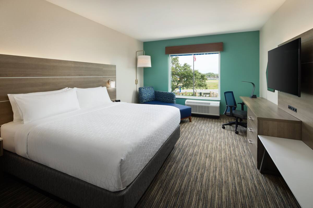 Une chambre d’hôtel avec un grand lit, un bureau, une chaise, une télévision et une fenêtre donnant sur l’extérieur.