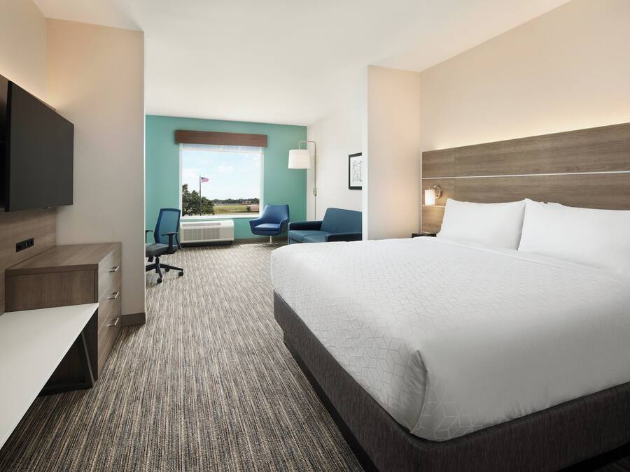 A hotel room with a large bed, a desk, a chair, a TV, and a window with a view.