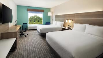 A hotel room with two beds, a desk, a chair, a TV, and a window with a view of trees.