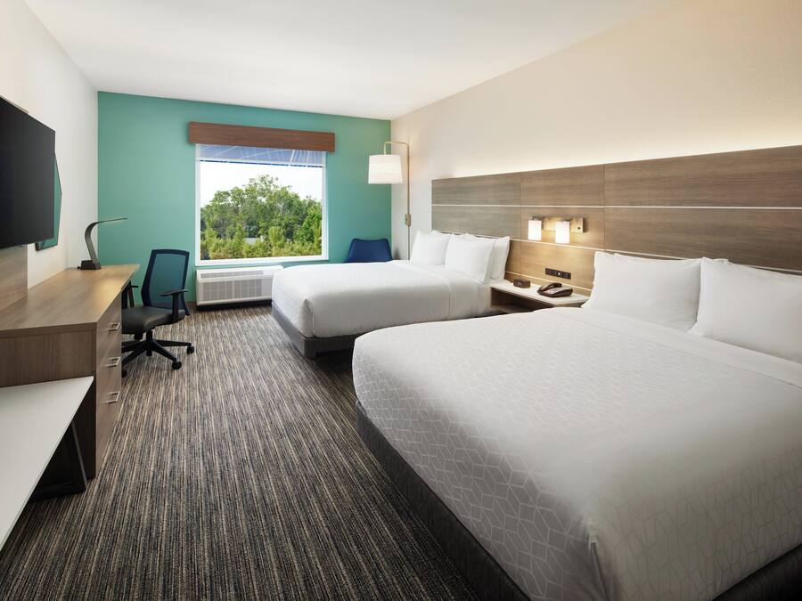 A hotel room with two beds, a desk, a chair, a TV, and a window with a view of trees.